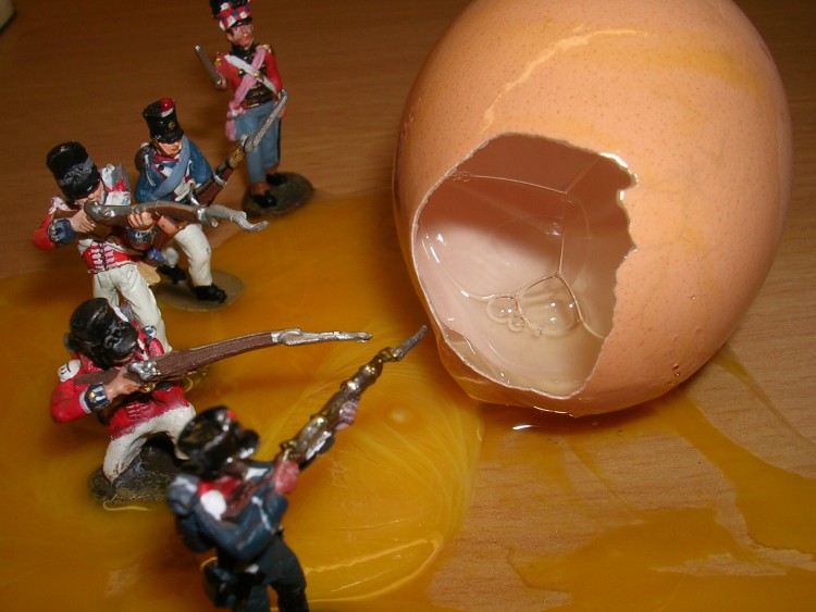 foto ironica di soldatini di plastica con il fucile puntato verso un uovo dalla cui frattura del guscio fuoriesce il tuorlo