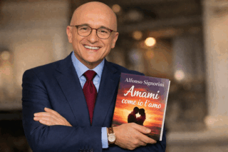 Alfonso Signorini sorridente con in mano il suo ultimo libro "Amami come io t'amo"